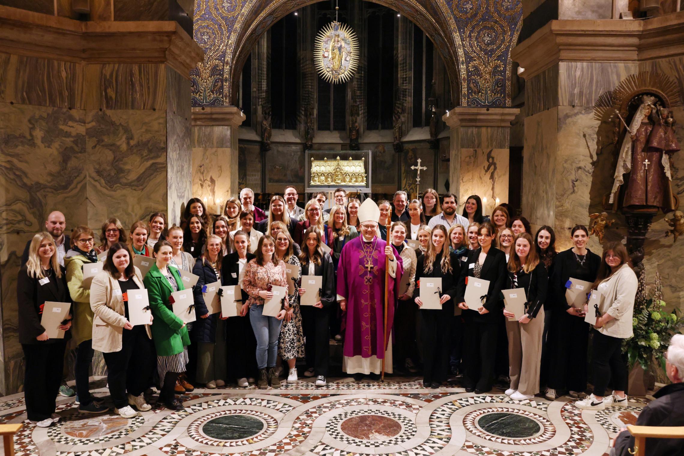 Menschen mit Urkunden in der Hand  stehen um Bischof Dieser im Aachener Dom vor dem Altar