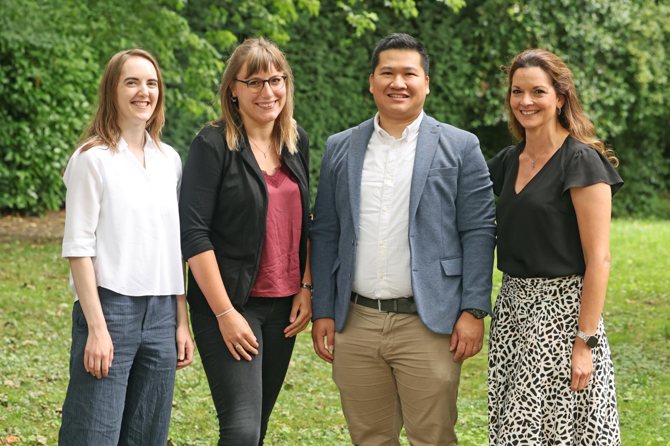 Anna Zimmermann, Vivien Bretz, Nadine Mihm und Peter Nguyen haben ihre Ausbildung im pastoralen Dienst im Bistum Aachen abgeschlossen. Vier Personen stehen auf grüner Wiese, sommerlich leger bis chic gekleidet
