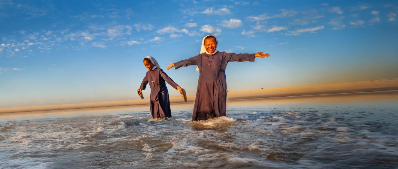 Frau steht im Wasser unter blauem Himmel, lchelt freundlich und streckt die Arme aus