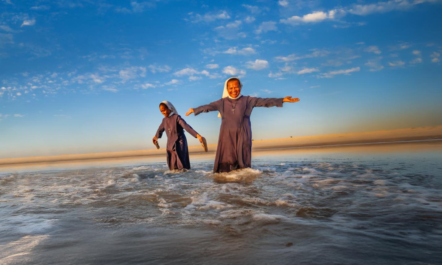 Frau steht im Wasser unter blauem Himmel, lchelt freundlich und streckt die Arme aus