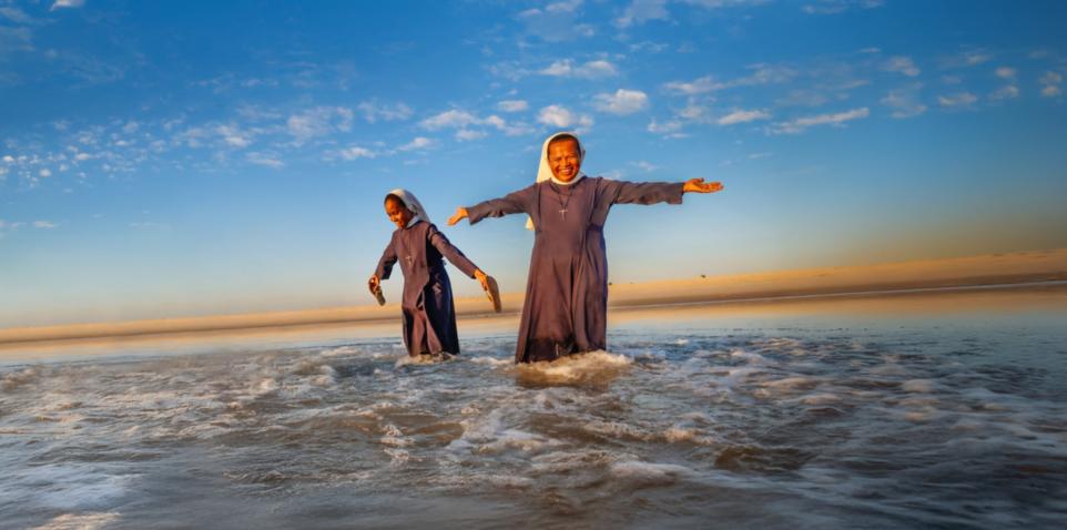 Frau steht im Wasser unter blauem Himmel, lchelt freundlich und streckt die Arme aus