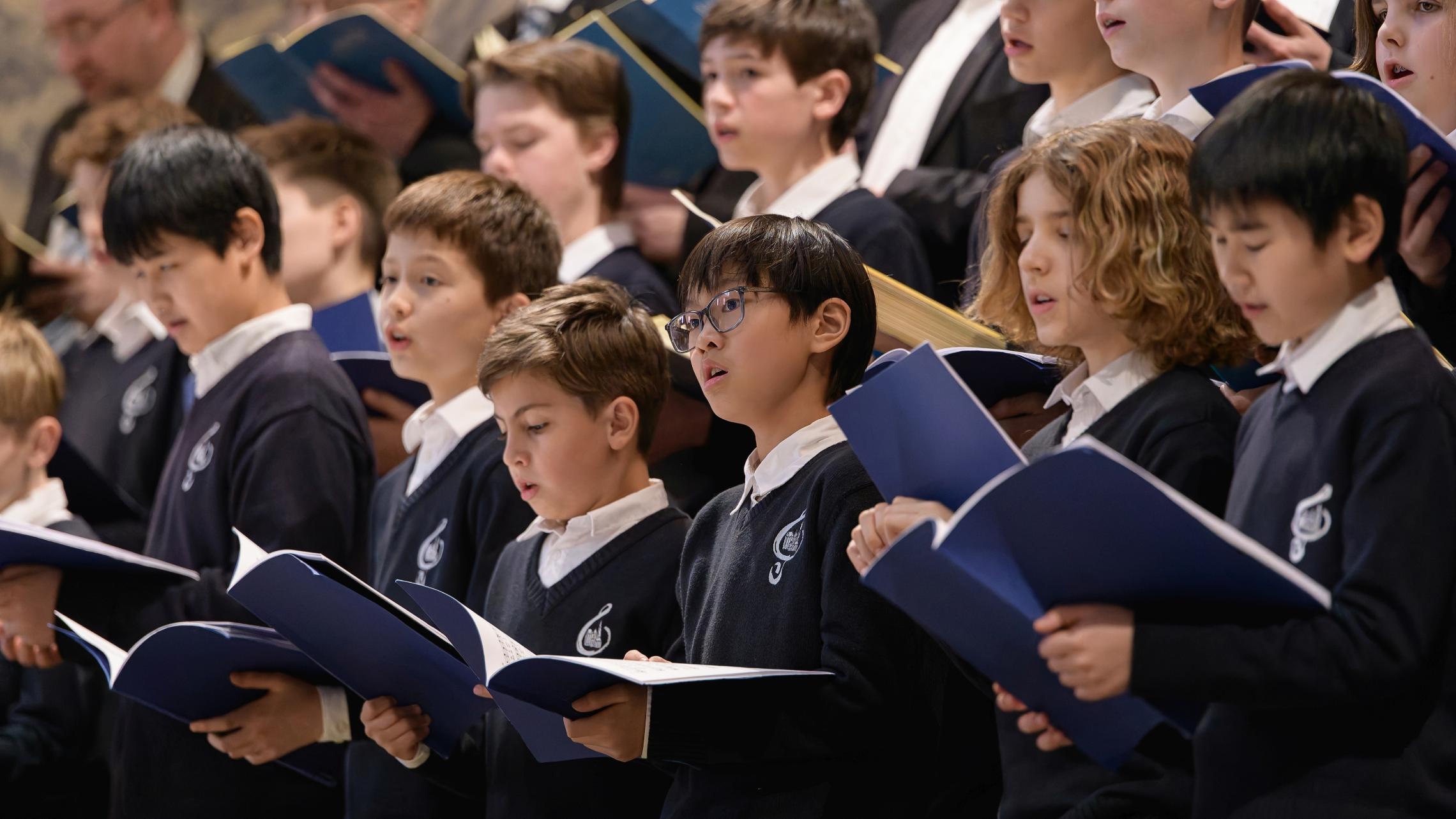 Kinder singen im Chor mit blauen Mappen und blauen Kleidern