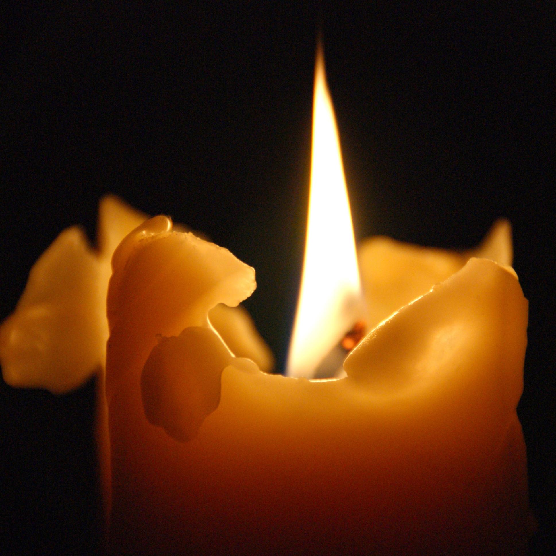 Brennende Kerze mit warmem Licht vor dunklem Hintergrund.