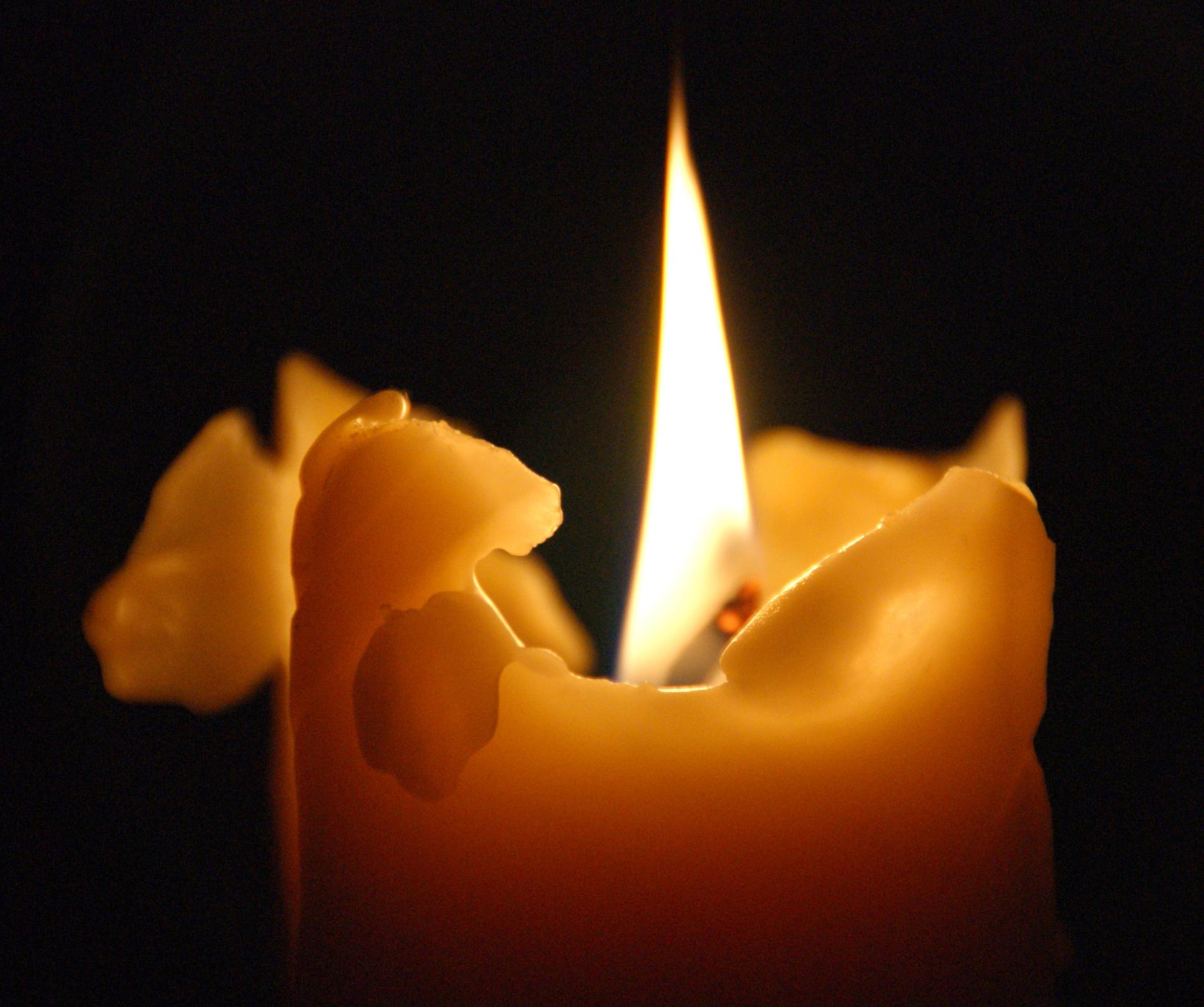 Brennende Kerze mit warmem Licht vor dunklem Hintergrund.