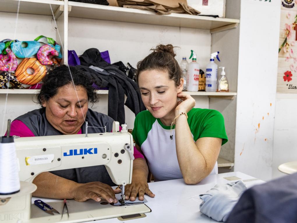Die Bochumer Schauspielerin Friederike Becht schaut Susana Raquel Guiller Alegría von der Asociación Papico beim Nähen über die Schulter. Nachdem eine Ölpest den Fischern die Lebensgrundlage entzogen hatte, hat Susana mit anderen Frauen die Initiative ergriffen. Die Teilnehmerinnen ihrer Nähkurse erhalten Zertifikate, sodass sie auch normierte Produkte wie Schulkleidung anbieten und so mehr Geld verdienen können.