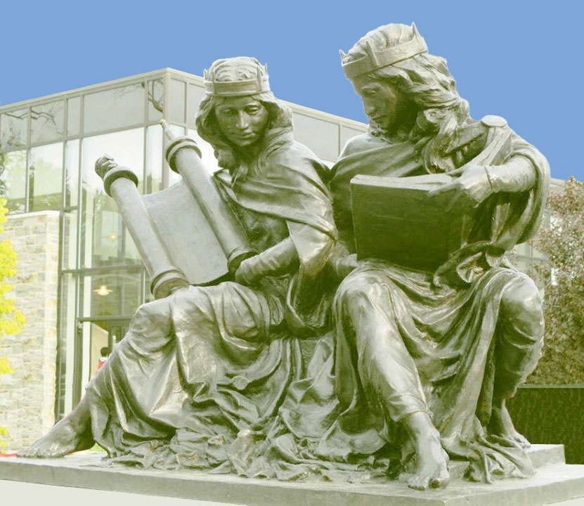 Bronzeskulptur. Nebeneinander sitzen zwei Frauen, eine mit einer Torarolle verkörpert die Synagoge, die andere mit einer Bibel verkörpert die Bibel.