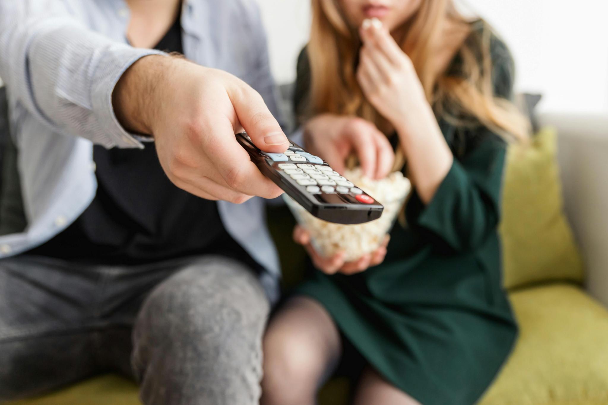 Mann und Frau auf dem Sofa mit Fernbedienung und einer Schüssel Popcorn.