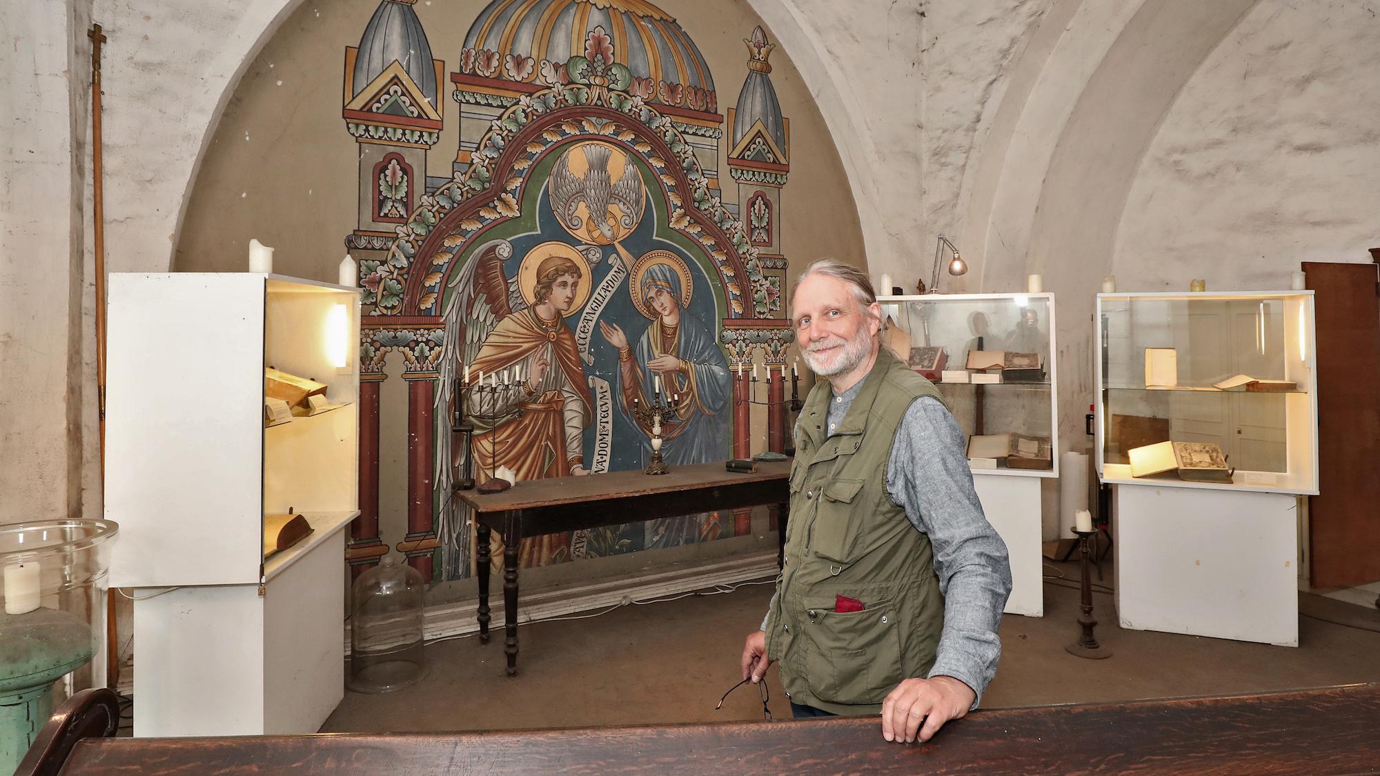 Kirchenvorstand Jürgen Schram in der Hasenaeckerschen Bibliothek in St. Josef. Das Wandbild zeigt Mariä Verkündigung.