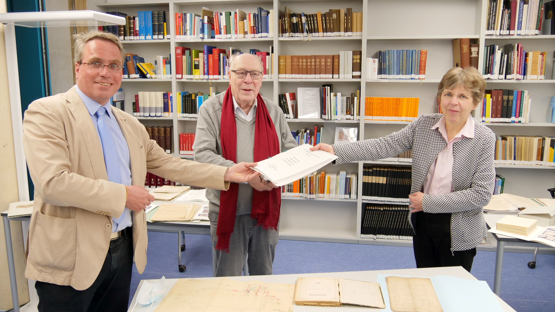 Übergabe im Diözesanarchiv: Dr. Peter Nieveler (M.) und Pfarrer Josef Wolff (l.) nehmen das Findbuch von Dr. Beate Sophie Fleck, Leiterin des Diözesanarchivs Aachen, entgegen.