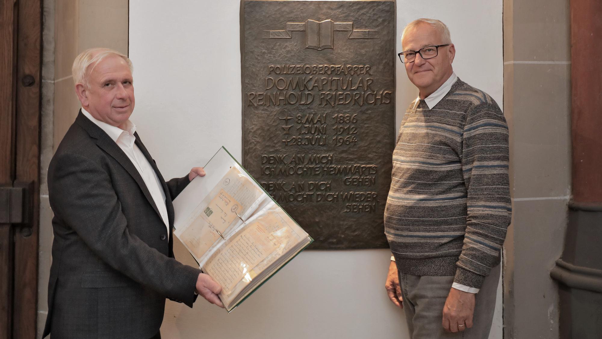 Pfarrer Paul Jansen (l., mit den Originalbriefen) und Gregor  Micus vor der Grabplatte von Domkapitular Reinhold Friedrichs.