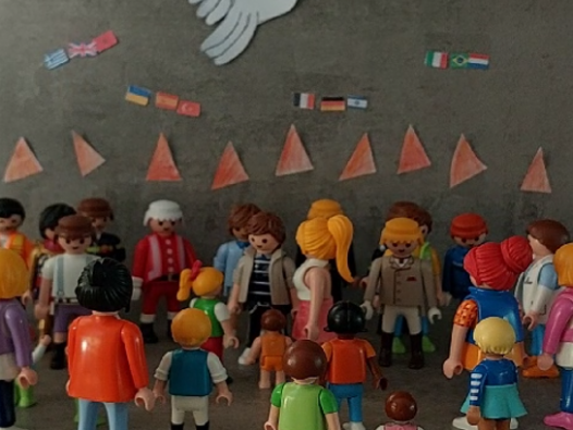 Viele Playmobilmännchen stehen zusammen. Über ihnen Feuerzungen und am Himmel eine weiße Taube.