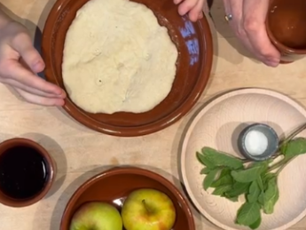 braune Teller mit Brotfladen, Äpfel, Salz und Bitterkräutern. Hände die den Teller halten und eine andere Hand, die den Becher mit Wein hält.