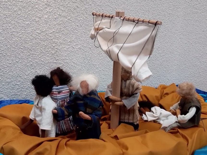 Biblische Erzählfiguren in einem Boot mit Segel. Jesus liegt im hinteren Teil und schläft am Boden.