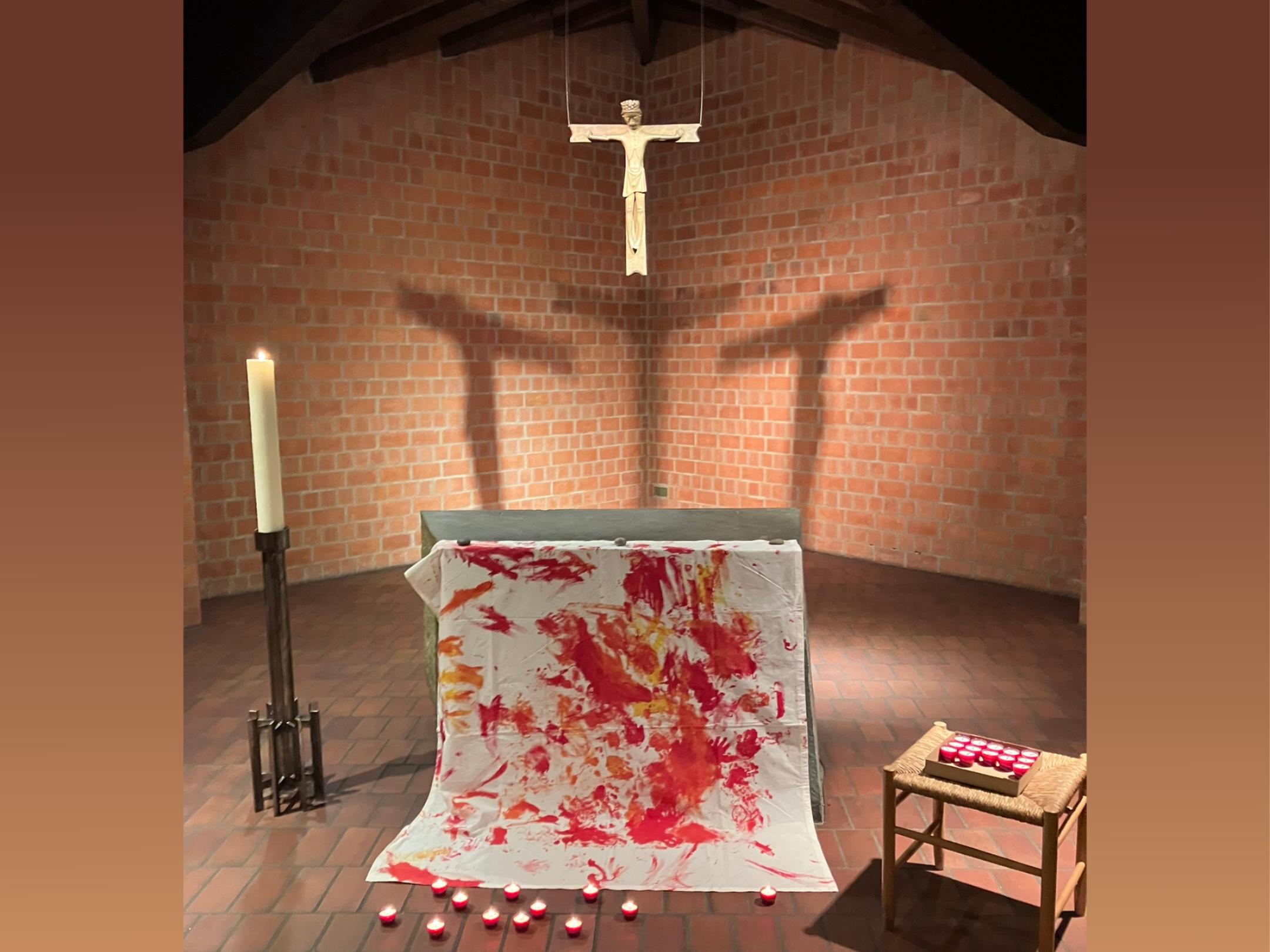 vor dem Altar: weißes Tuch mit roten Flecken, davor: brennende rot Teelichter