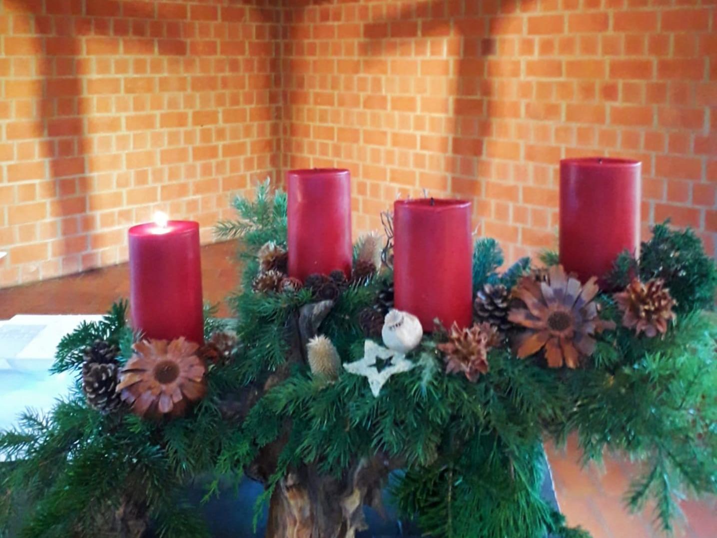 Adventskranz mit vier roten Kerzen, eine brennend