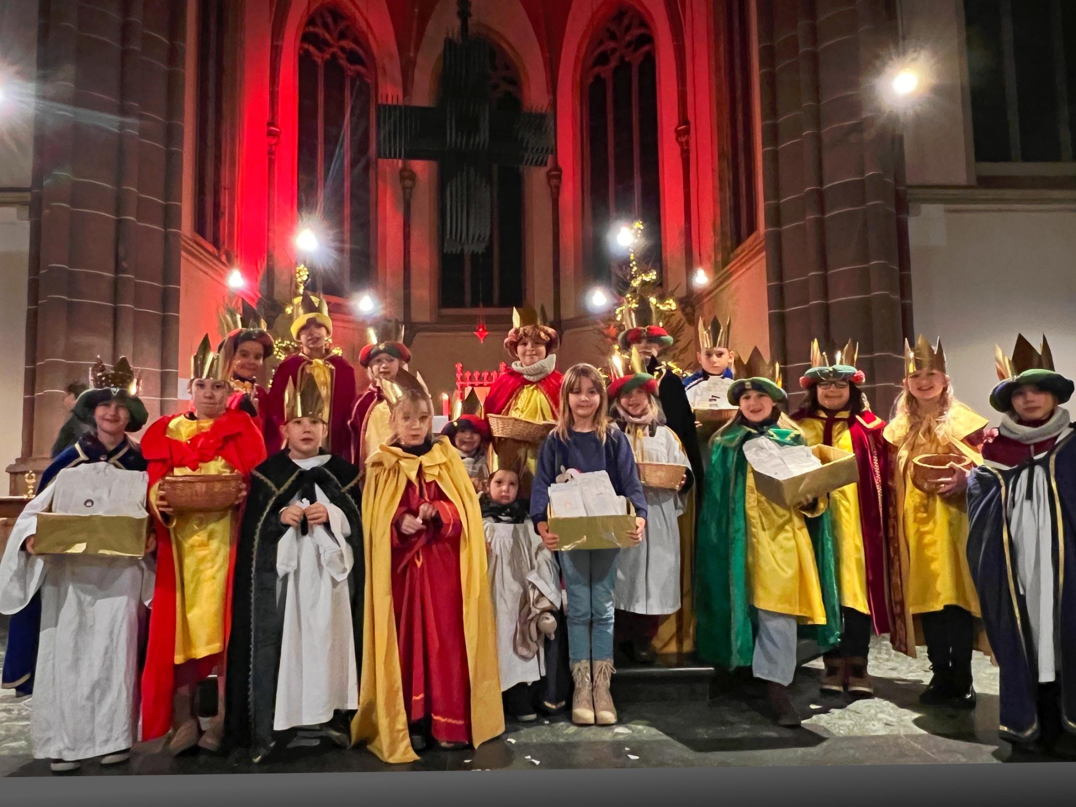 Kinder stehen als Sternsinger:innen in einer großen Gruppe auf den Stufen vor dem Altar der Schutzengelkirche